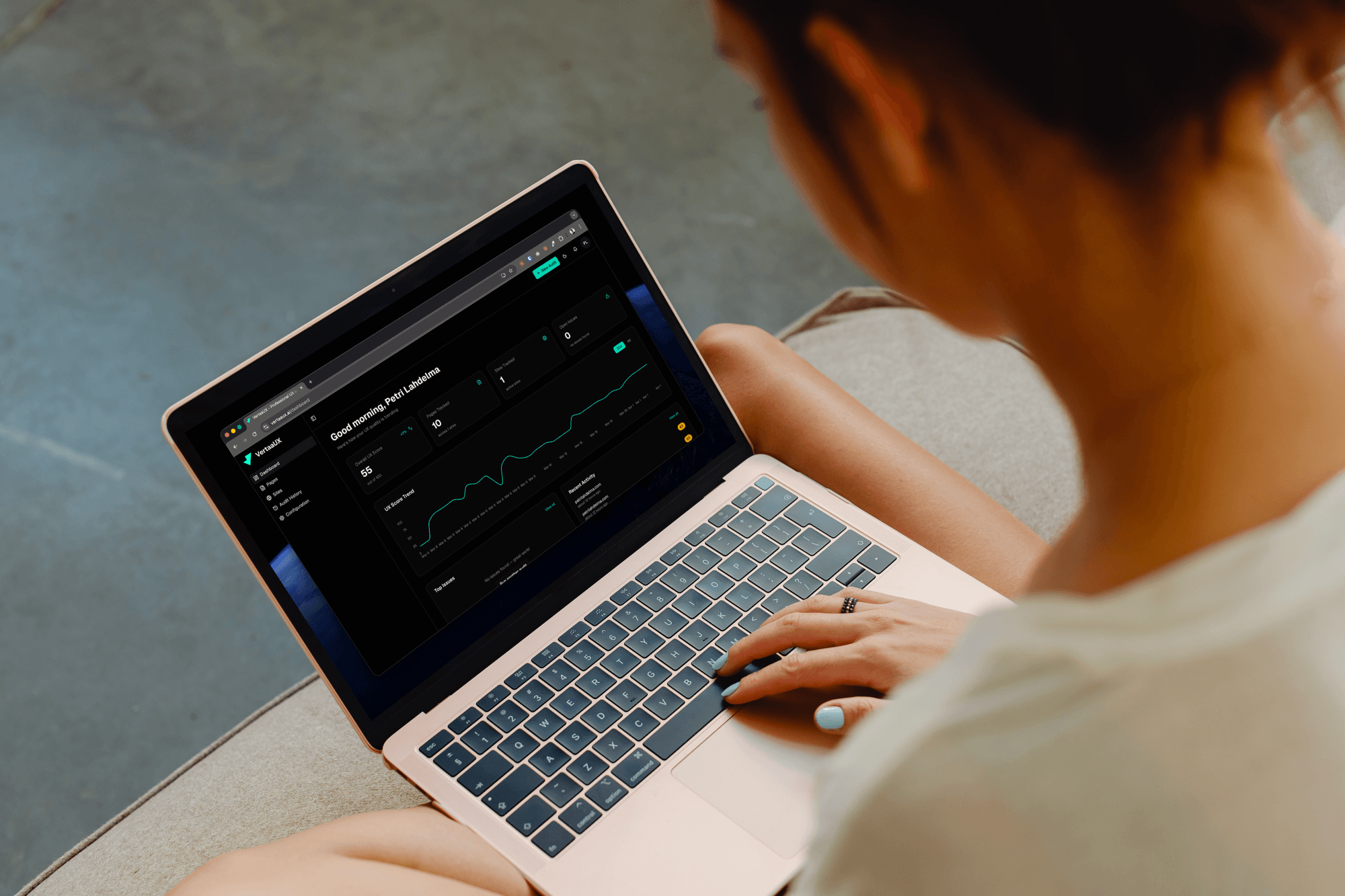 Person using VertaaUX dashboard on a laptop, showing score trends, audit history, and team activity